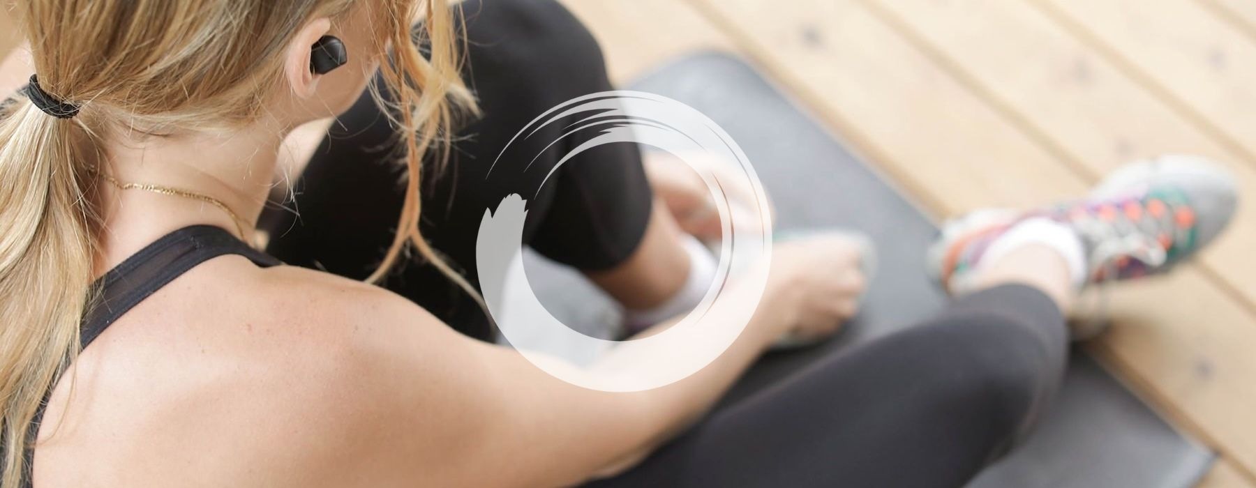 woman in workout gear, sits on a yoga mat and ties her shoe
